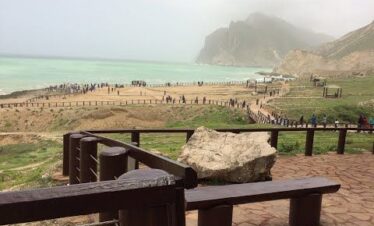 Wide panoramic view of Mughsail Beach with sandy shore and rocky cliffs