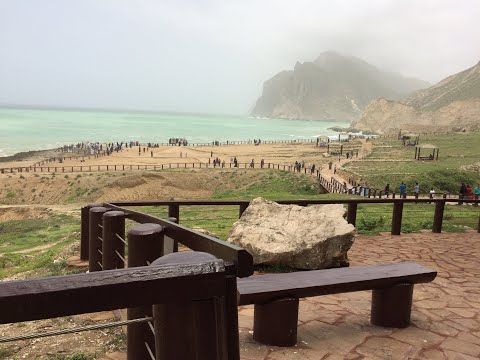 Wide panoramic view of Mughsail Beach with sandy shore and rocky cliffs