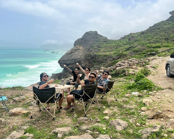 Group of people enjoying the sunset view from a cliff at Mughsail Beach