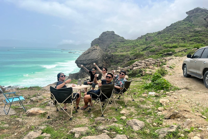Group of people enjoying the sunset view from a cliff at Mughsail Beach